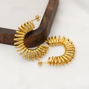 Macro shot of gold-plated stainless steel spiral spring hoop earrings on a wood tray