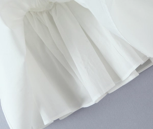 Close-up of white dress hem featuring delicate floral embroidery and ruffled pleats