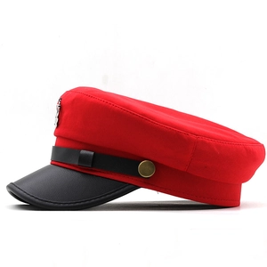 Detail of red fabric beret with black leather brim, gold buttons, and metal anchor emblem