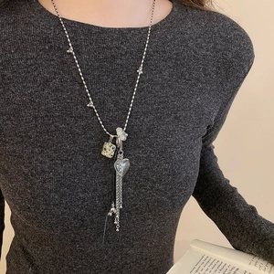 Dettaglio di una collana lunga con cristallo a cuore e nappa su un maglione grigio