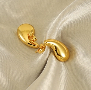 Macro di orecchini a goccia d'oro lucido su sfondo di seta di lusso elegante