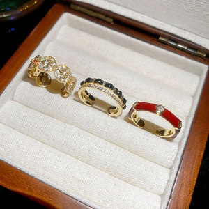 Three 14k gold-plated rings with zircon and red enamel on a wooden jewelry display