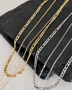 Close-up of gold and silver layering necklaces with Figaro links on a black stone