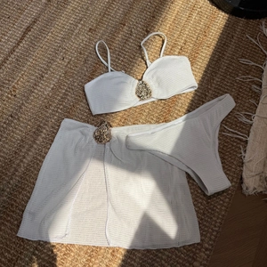 Detail of white crochet bikini with honeycomb texture and golden metallic buckle accents