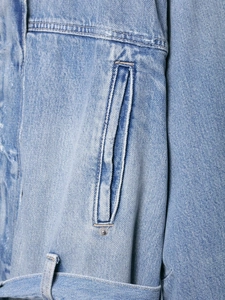 Detailed close-up of light blue denim jacket pockets with vintage wash and reinforced stitching