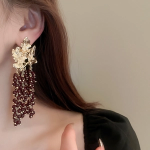 Close-up of vintage golden leaf earrings with dark red beaded tassels on a female model
