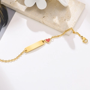 Détail d'un bracelet doré ajustable avec plaque d'identification et petit pendentif cœur