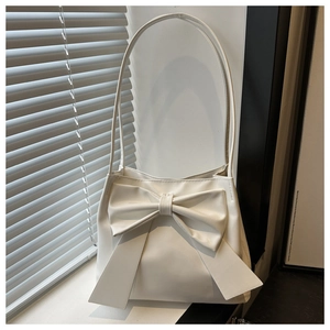 Detailed close-up of a white minimalist shoulder bag with a large bow decoration