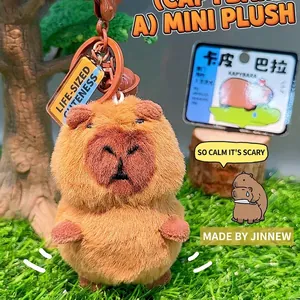 Cute brown capybara plush keychain with metal ring and small bell on grass background