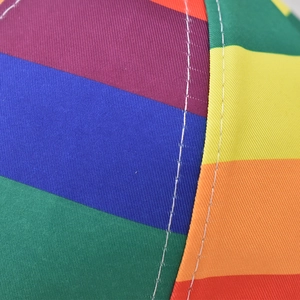 Macro shot showing white stitching on colorful rainbow striped fabric of the baseball cap