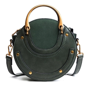 Detail of dark green round crossbody bag featuring suede texture and gold ring handle