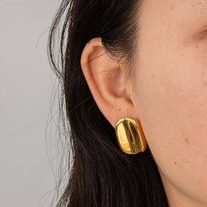 Close-up of polished gold-plated oval hoop earrings worn for a minimalist vintage aesthetic