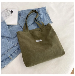 Army green thick canvas tote bag styled on white bedding with a blue denim jacket