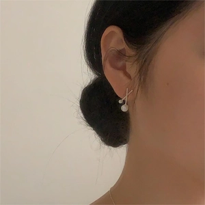 Minimalist silver pearl earring showing a crisscross design on woman's ear