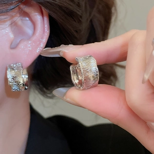 Close-up of wide silver earrings featuring irregular wavy texture and polished finish