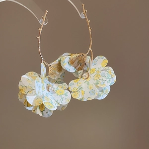 Detailed macro view of golden branch earrings with fabric floral elements and faux pearls