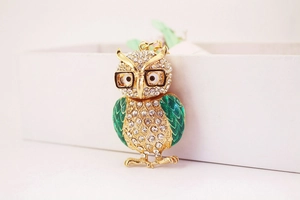 Détail d'un porte-clés chouette doré avec ailes en émail vert et strass scintillants