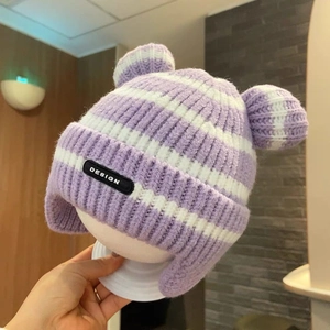 Detail of purple and white striped knit baby hat with ear flaps and cute pom-poms