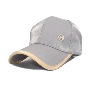 Detail of silver satin baseball cap featuring a metallic M logo and beige piped brim