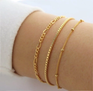 Nahaufnahme eines goldfarbenen Figaro- und Perlenarmband-Sets am Handgelenk