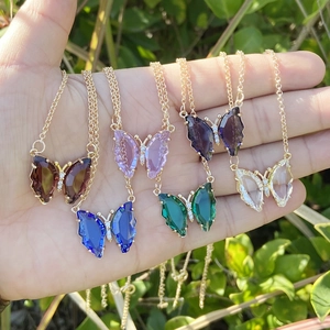Multiple butterfly necklaces with colorful crystal pendants held in palm on gold chains