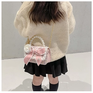 Detail of pink tweed girl's handbag featuring a satin bow and pearl handle with chain strap