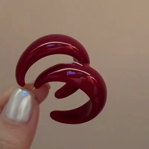 Detailed close-up of dark red C-shaped acrylic earrings with a glossy resin finish