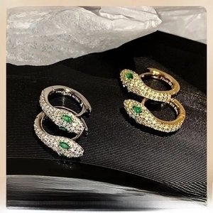 Macro detail of snake hoop earrings featuring pavé crystals and green emerald-like eyes