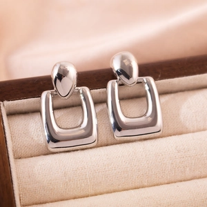 Polished silver geometric earrings with teardrop studs and square hoops on beige velvet