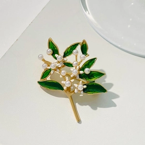 Macro detail of leaf brooch with green enamel, white flowers and faux pearls