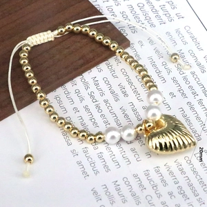 Macro detail of hand-woven beaded bracelet with gold beads, pearls and 20mm heart charm