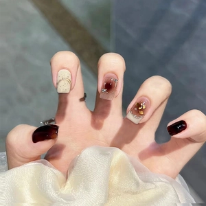 Macro detail of burgundy and white press-on nails with glitter bow and gold foil accents