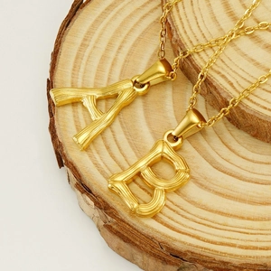 Close-up of golden stainless steel A and B initial pendants on rustic wood base