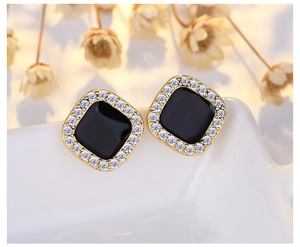 Macro shot of gold square stud earrings with black enamel and sparkling zircon border