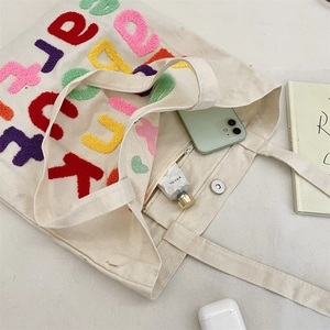 Detail of canvas tote bag with colorful bouclé letter embroidery and magnetic snap closure