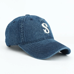 Close-up of white letter S embroidery on washed dark blue denim baseball cap
