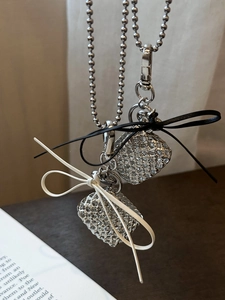 Detail of silver cubic bag pendants with black and white leather bows on beaded chains
