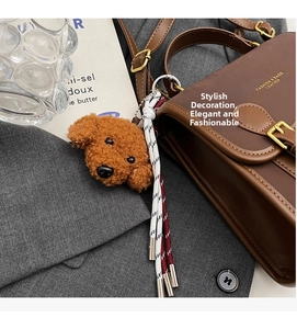 Detail of a brown plush poodle charm with woven red and white rope on a leather handbag