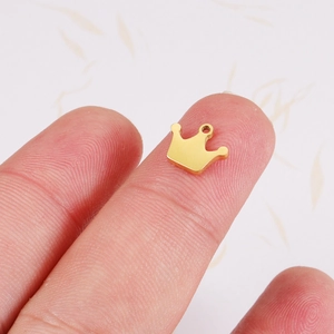 Polished gold stainless steel crown pendant accessory shown on a fingertip for scale