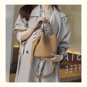 Detailed view of caramel leather bucket bag with checkered scarf and textured finish