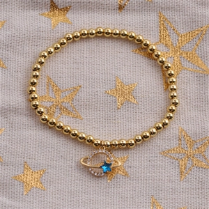 Gold beaded Saturn bracelet with a sparkling blue star pendant on a starry beige background