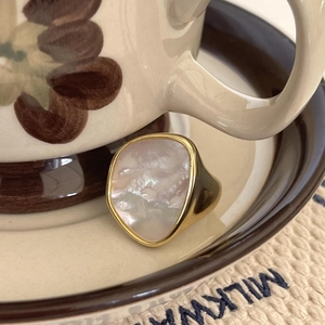 Close-up of a 925 silver gold-plated ring with iridescent mother of pearl on a vintage saucer