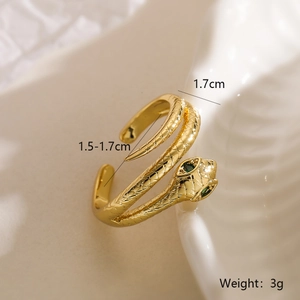 Macro shot of gold snake ring with scale textures and green zircon eyes on soft fabric