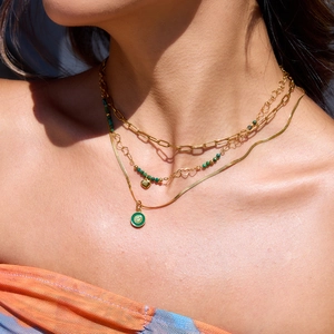 Detailed view of triple-layered gold necklace with green stones and heart pendants on model