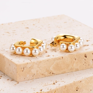 Vintage 18K gold square C-shaped pearl hoop earrings displayed on a textured stone stand