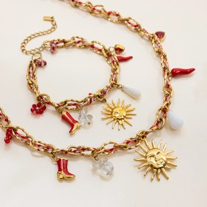 Detail of gold chain necklace with red braided cord and assorted charms like a sun and boot