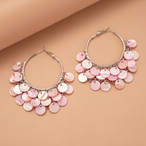 Macro detail of silver hoop earrings featuring layered pink shell disc tassels on pink background
