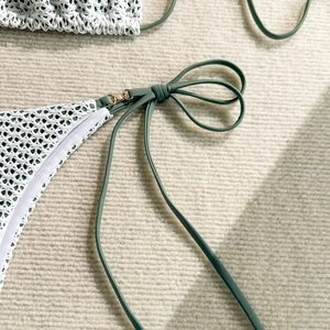 Detail of white crochet bikini with dark green lining, gold rings and pearl accents
