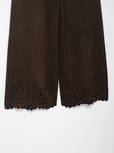 Détail du pantalon en daim marron foncé avec motifs floraux découpés au laser et bord festonné