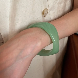 Close-up of minimalist bean green resin bangle worn on wrist with natural soft lighting